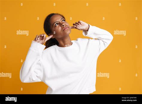 Brunette Black Girl Looking Upward While Plugging Her Ears Isolated Over Yellow Background Stock