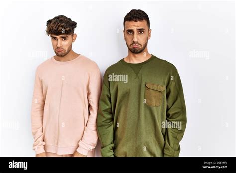 Jeune couple gay debout sur fond blanc isolé déprimé et s inquiéter de