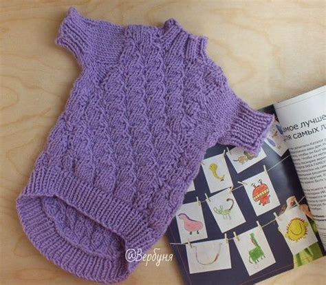 a purple knitted sweater sitting on top of a table next to an open book