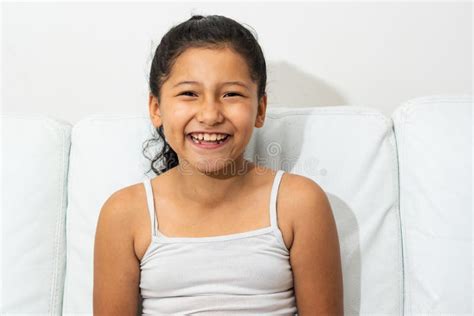 Portrait Of A Latin Brunette Girl Sitting On The Sofa Smiling And Showing Her Teeth Stock Photo