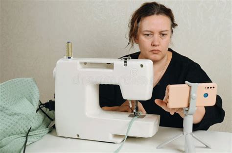 A Female Seamstress Sews Green Fabric Items On A Sewing Machine Stock