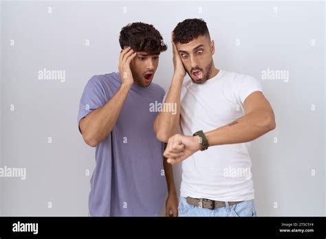 Homosexual Gay Couple Standing Over White Background Looking At The Watch Time Worried Afraid