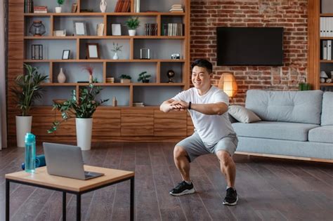 Premium Photo Happy Athlete Asian Mature Man In Sports Clothes Squatting In Living Room