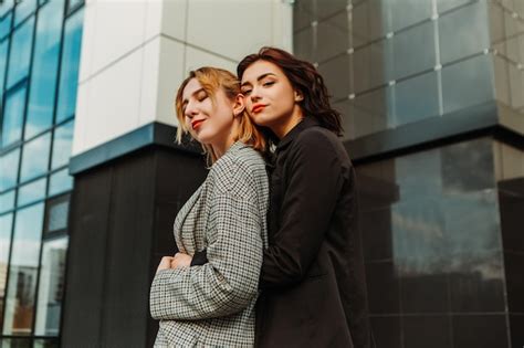 Dos amigas bonitas posando cerca de un edificio de cristal pareja de gay lesbianas niñas