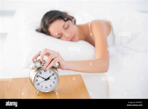 Calm Casual Brunette In White Pajamas Turning Off Her Alarm Clock Stock