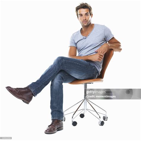 Portrait Of Young Man Sitting On Chair With Legs Crossed Against White