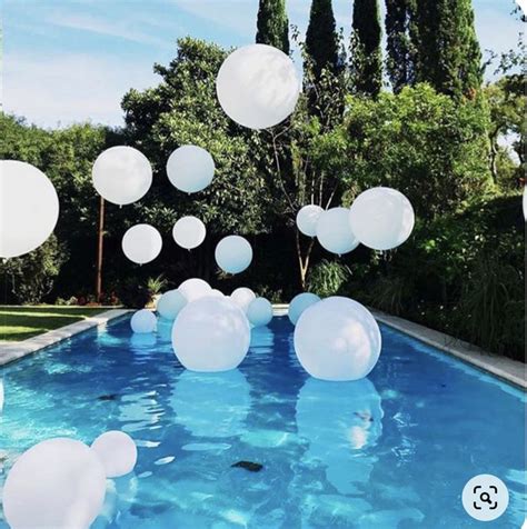 White Balloons Floating In The Air Over A Swimming Pool With Blue Water