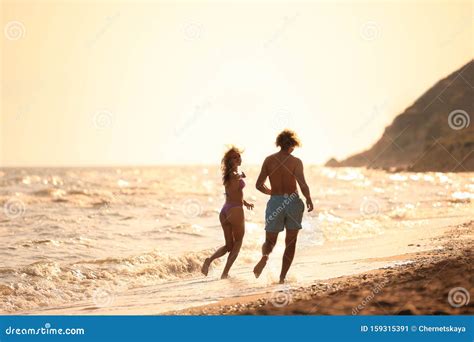 Jeune Femme En Bikini Et Son Petit Ami S Amusant Sur La Plage Au Coucher Du Soleil Image Stock