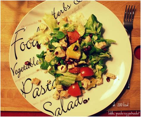 A White Plate Topped With Salad On Top Of A Wooden Table Next To A Fork