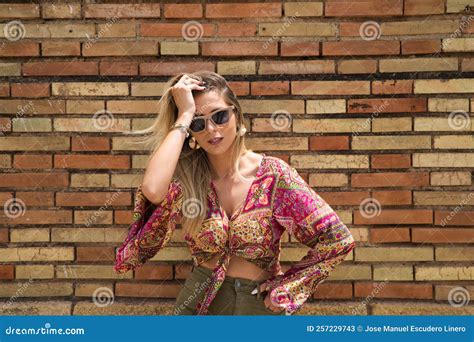 Jeune Blonde Belle Femme Avec Lunettes De Soleil Pose Sur Fond De Brique Rouge Tout En Touchant