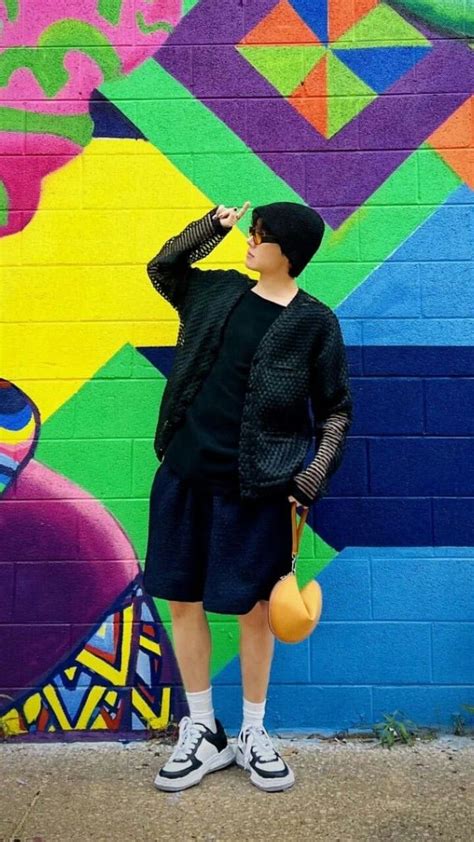 A Man Standing In Front Of A Colorful Wall Drinking From A Yellow Cup