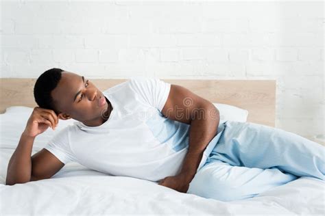 African American Man Looking Away Laying On Bed In White Room Stock