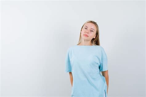 Femme blonde debout tout droit et se présentant à la caméra en t shirt bleu et ayant l air
