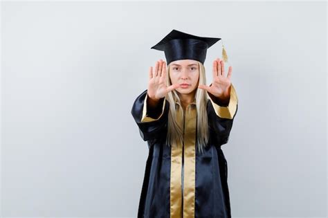 졸업 가운과 모자에 정지 신호를 표시 하 고 심각한 찾고 금발 소녀 무료 사진