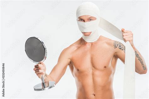 Naked Man Taking Off Bandages From Head After Plastic Surgery And Holding Mirror Isolated On