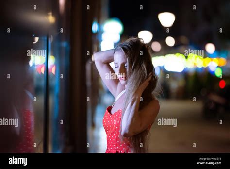 Portrait Of A Beautiful Mature Woman In A Red Dress While Checking The Storefront At Night With