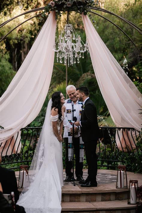 A Bride And Groom Standing Under A Chandelier At Their Wedding Ceremony