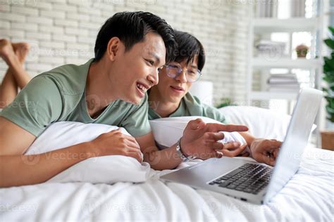 feliz pareja gay asiática usando laptop y relajándose en casa en la cama concepto lgbtq