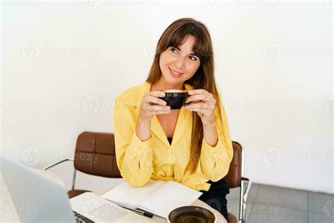 Smiling Brunette Woman In Yellow Blouse Using Lap Top And Drinking Coffe In Modern White