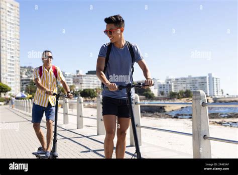 Heureux Biracial Gay Couple M Le Cheval Scooters Sur La Promenade Au