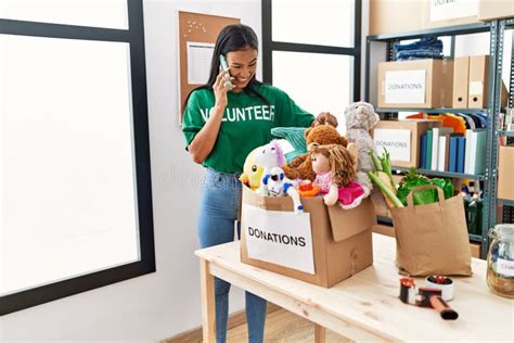 Joven Latina Con Uniforme De Voluntaria Hablando En El Smartphone Del Centro De Caridad Foto De