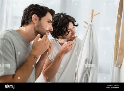 Blurred And Tattooed Gay Man Touching Face While Boyfriend Brushing