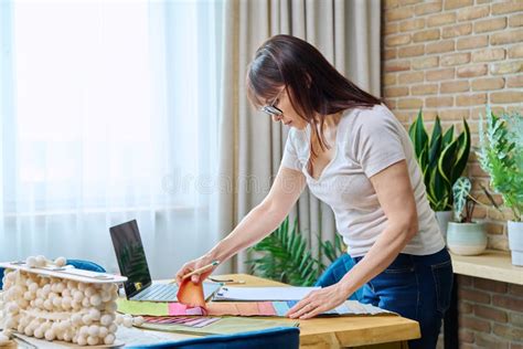 Mature Woman Interior Designer Working At Her Desk With Fabric Samples Laptop Stock Photo