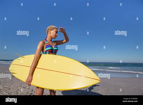 Beautiful Woman In Bikini With Surfboard Shielding Eyes On Beach In The