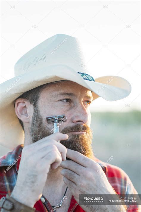 Portrait Of Bearded Man In Cowboy Hat Shaving With Vintage Double Edge