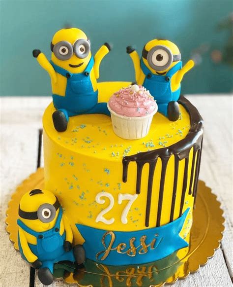 a yellow cake with two minion figures on top and a frosted cupcake in ...