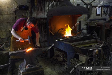 Female Blacksmith Striking Red Hot Metal On Anvil Inside Workshop Industrial Facility Apron