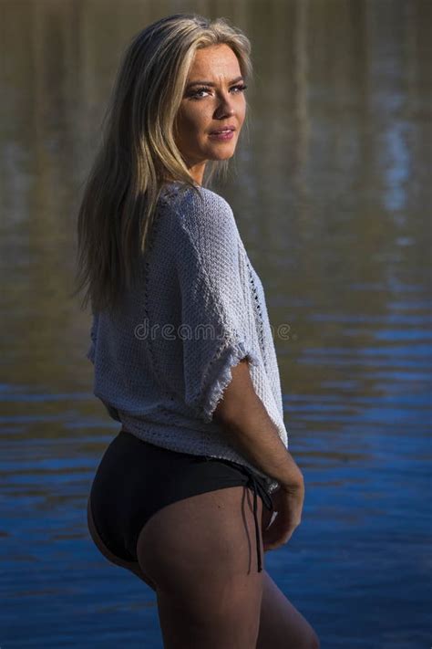 A Lovely Blonde Bikini Model Poses Outdoors Near A Lake While Enjoying The Summer Weather Stock