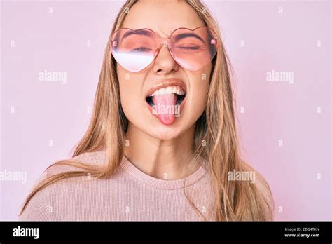 Jeune Belle Femme Blonde Portant Des Lunettes De Soleil En Forme De Coeur Qui Collent La Langue