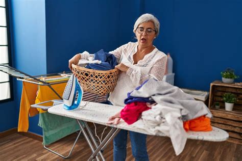 Middle Age Woman Stressed Doing Chores At Laundry Room Stock Photo