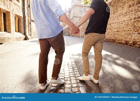 Rear View Of Male Gay Couple On Vacation Holding Hands Walking Along City Street Stock Image
