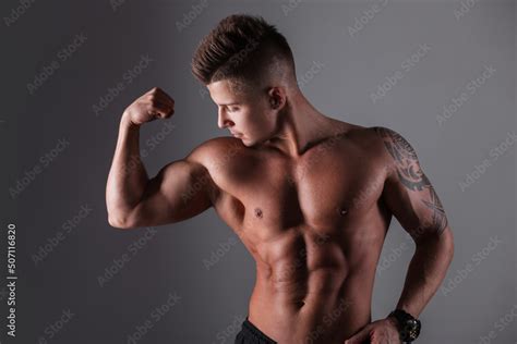 Sporty Handsome Guy Bodybuilder Model With A Healthy Naked Muscular Torso Shows His Biceps On A
