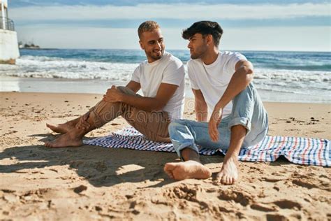 Jovem Casal Gay Sorrindo Feliz Sentado Na Praia Foto De Stock Imagem De Relacionamento