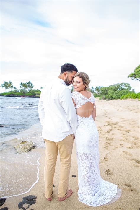 A Bride And Groom Standing On The Beach In Front Of The Ocean Looking