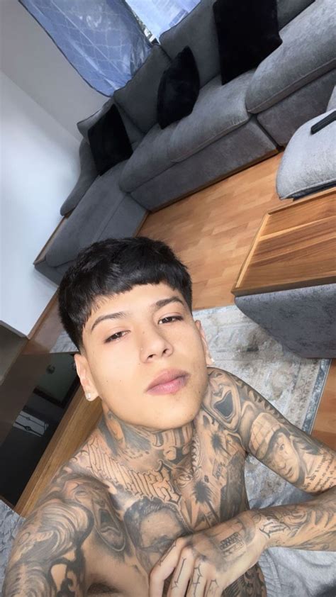 A Man With Tattoos On His Chest Sitting In Front Of A Couch And Looking