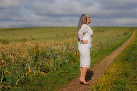 Elegant Mature Woman In White Dress Standing In Profile On A Path In The Countryside Stock Photo
