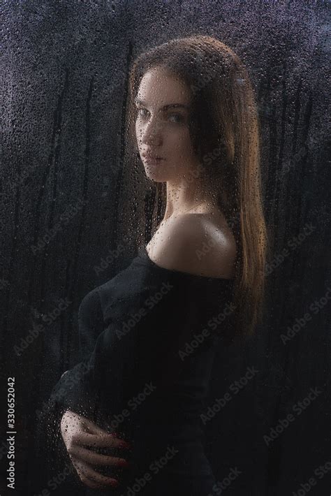 Beautiful Slender Brunette In A Black Dress With A Good Figure Behind The Glass With Raindrops