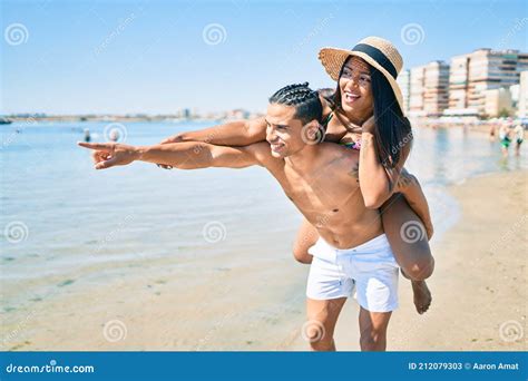 Joven Pareja Latina Abrazándose Y Señalando El Horizonte Con El Dedo a La Playa Imagen de