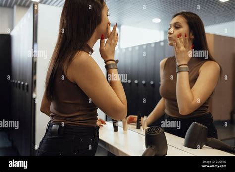 Beautiful Brunette Sporty Woman Applying Face Cream Looking In The Mirror In Dark Gym Locker