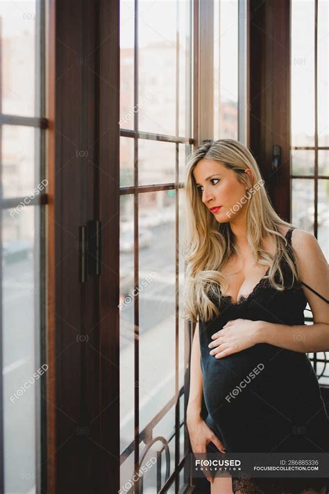 Thoughtful Pregnant Woman In Lingerie Standing Near Window At Home Leaning Dark Stock Photo