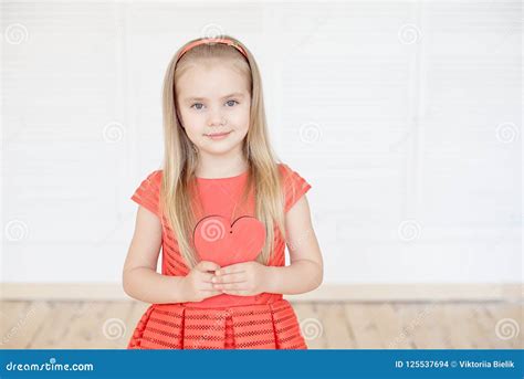 Jeune Petite Fille Blonde Portant Dans La Longue Robe Sans Manche Tenant Le Coeur Rouge De