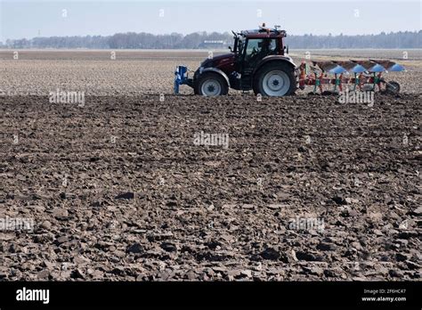 Landwirt im Traktor mit Pflug hinter ihm pflügt durch ein Feld aus