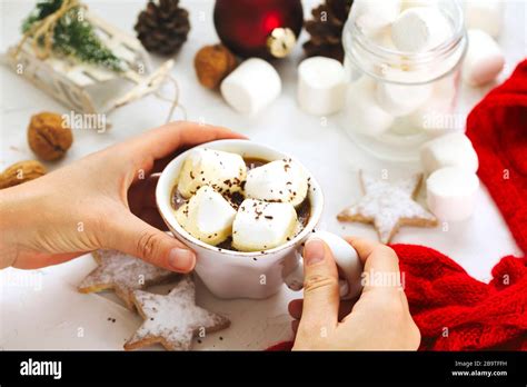 Female Hand Holding Cup Of Hot Chocolate With Marshmallow On White Table From Above Christmas