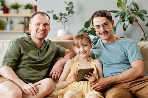 Retrato de familia gay sentado en el sofá con hija adoptiva mediante tableta digital en casa