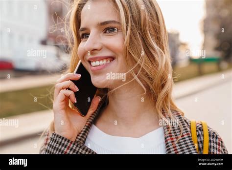 Jeune femme blonde souriante parlant sur un téléphone portable tout en se tenant dans une rue de
