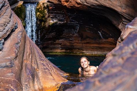 Ein mädchen in einem weißen bikini entspannt sich in einem felsenbecken mit einem wasserfall